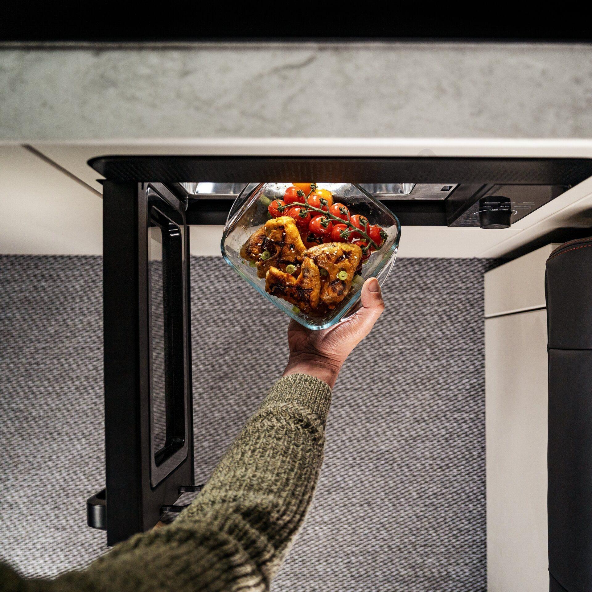 Personne plaçant un plat de nourriture dans le micro-ondes Dometic d’un van aménagé
